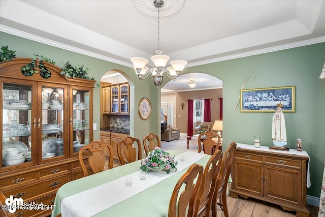 dining space with an inviting chandelier, a tray ceiling, ornamental molding, and light hardwood / wood-style floors