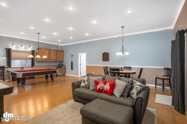 living room with crown molding, an inviting chandelier, and light wood-type flooring