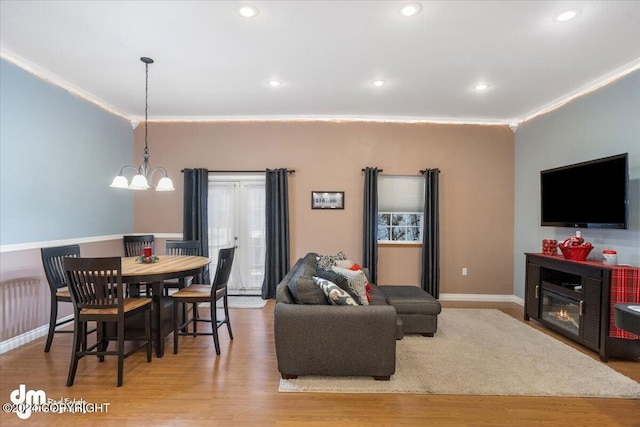 living room with crown molding, a chandelier, and light hardwood / wood-style flooring