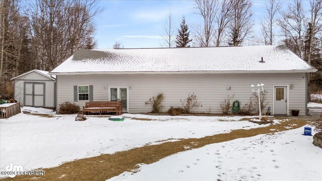 snow covered back of property featuring a deck and a storage shed