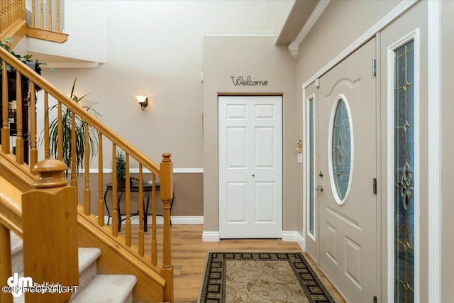 foyer featuring a towering ceiling, stairs, baseboards, and light wood-style floors