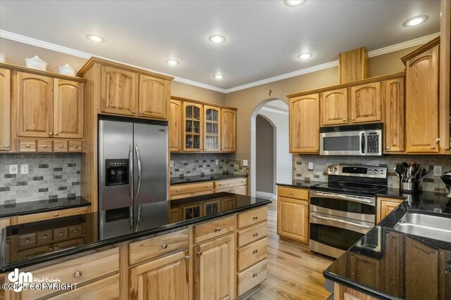kitchen with tasteful backsplash, arched walkways, appliances with stainless steel finishes, and crown molding