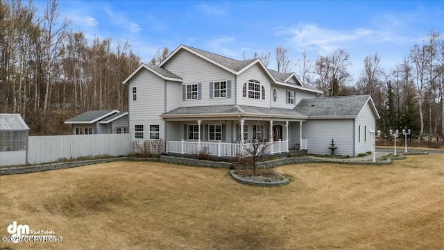 traditional-style home with a porch, a front yard, roof with shingles, and fence