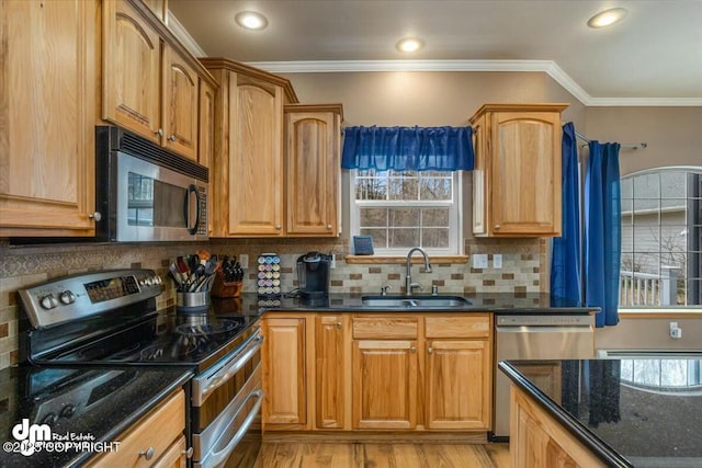 kitchen featuring dark stone countertops, a sink, appliances with stainless steel finishes, plenty of natural light, and light wood finished floors