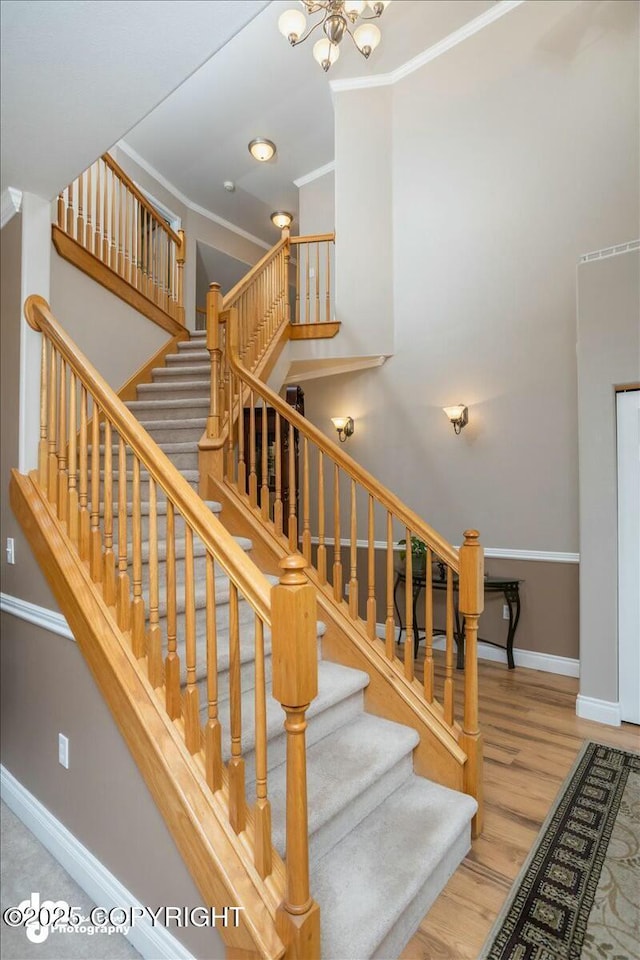 stairway with wood finished floors, a chandelier, ornamental molding, baseboards, and a towering ceiling