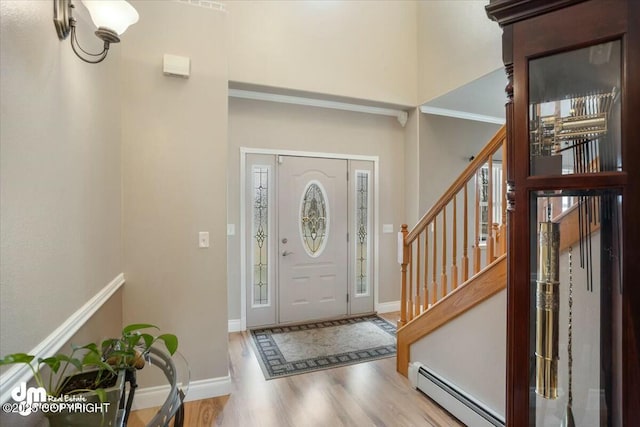foyer entrance featuring wood finished floors, stairs, baseboard heating, baseboards, and a towering ceiling
