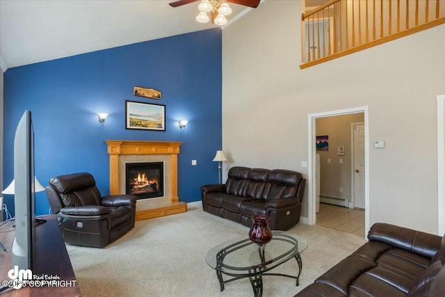 living area with carpet, baseboard heating, ceiling fan, a glass covered fireplace, and high vaulted ceiling