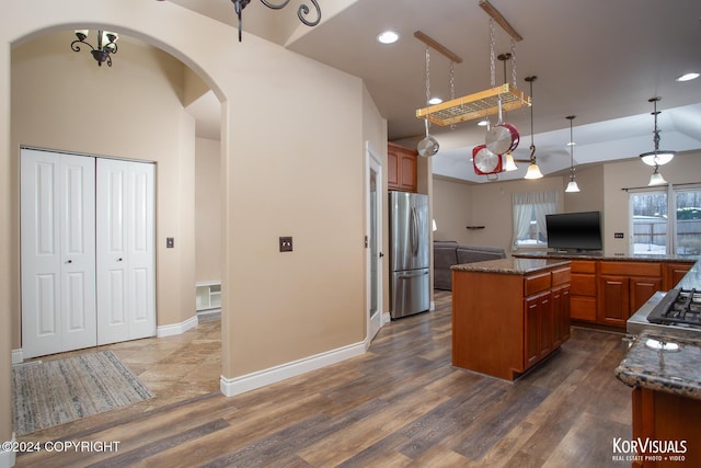 kitchen featuring dark stone countertops, stainless steel refrigerator, a center island, dark wood-type flooring, and stove