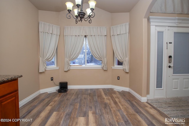 unfurnished dining area with lofted ceiling, an inviting chandelier, and dark wood-type flooring