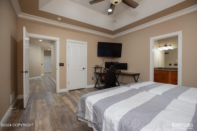 bedroom featuring connected bathroom, hardwood / wood-style floors, ceiling fan, and a tray ceiling