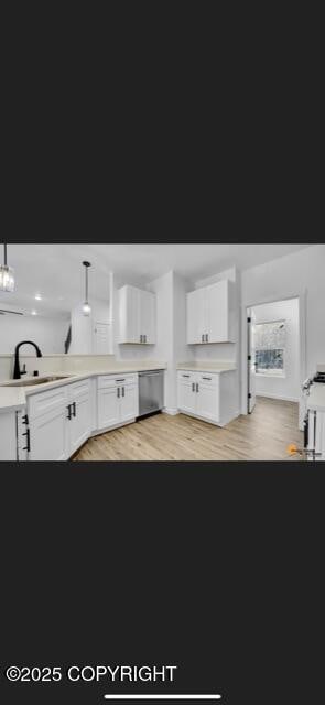 kitchen with pendant lighting, dishwasher, white cabinets, sink, and light hardwood / wood-style floors