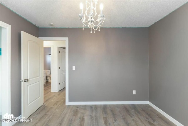 empty room featuring an inviting chandelier, a textured ceiling, and light wood-type flooring