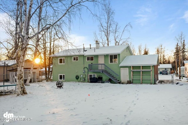 snow covered back of property with a trampoline, a garage, and a fire pit