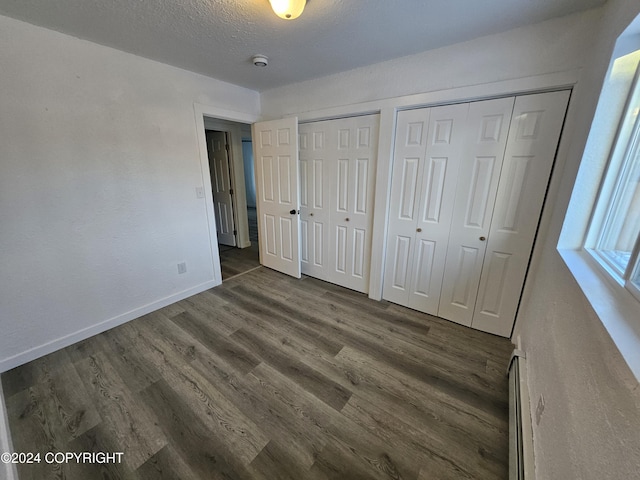 unfurnished bedroom featuring a textured ceiling, multiple closets, dark wood-type flooring, and a baseboard radiator