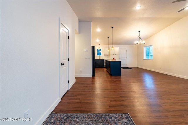 unfurnished living room with dark wood-type flooring, vaulted ceiling, and a notable chandelier