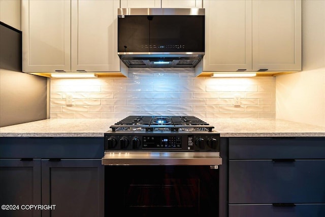 kitchen with tasteful backsplash, white cabinetry, light stone counters, and stainless steel range with gas stovetop