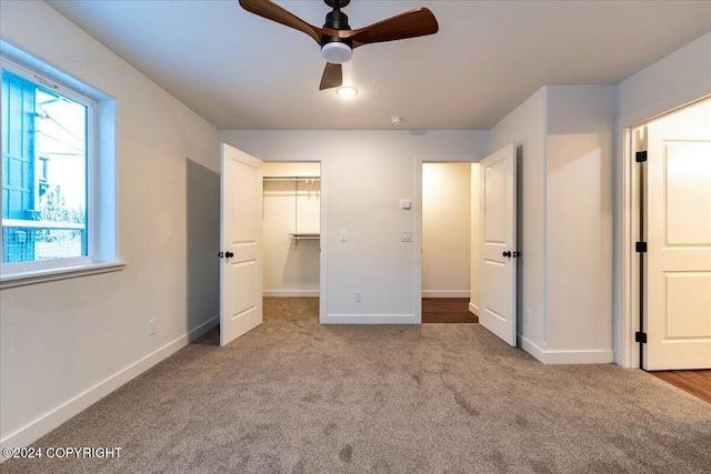 unfurnished bedroom featuring light carpet, a walk in closet, a closet, and ceiling fan