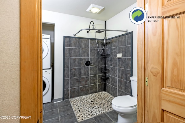 bathroom with tiled shower, tile patterned floors, stacked washer / dryer, and toilet