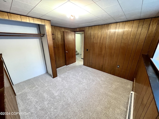 unfurnished bedroom featuring light colored carpet, a baseboard radiator, a closet, and wooden walls