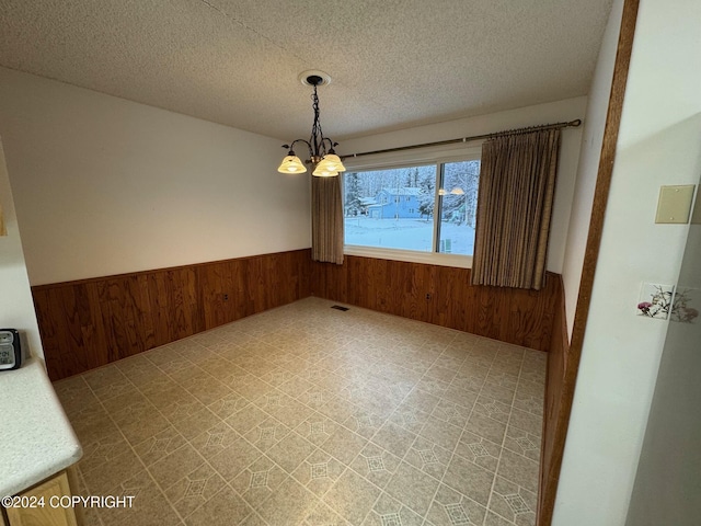 unfurnished dining area with a wainscoted wall, tile patterned floors, a textured ceiling, wood walls, and a notable chandelier