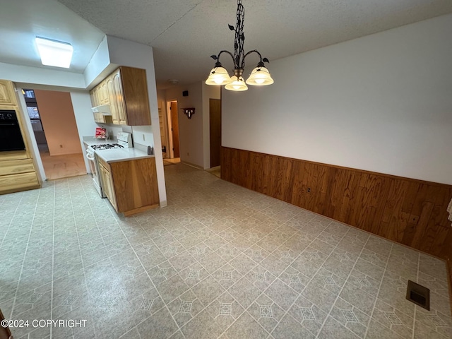 kitchen with white gas stove, oven, wood walls, light countertops, and wainscoting