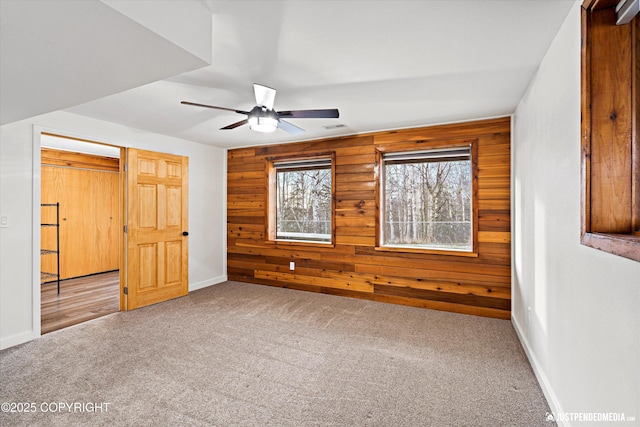 unfurnished bedroom featuring ceiling fan, light colored carpet, and wood walls