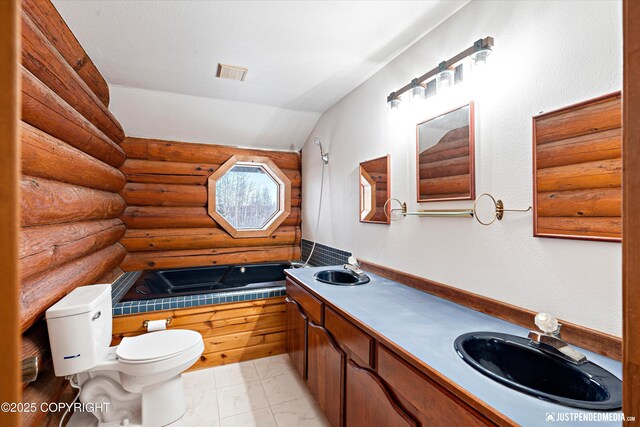 bathroom with toilet, rustic walls, vanity, and a bathing tub