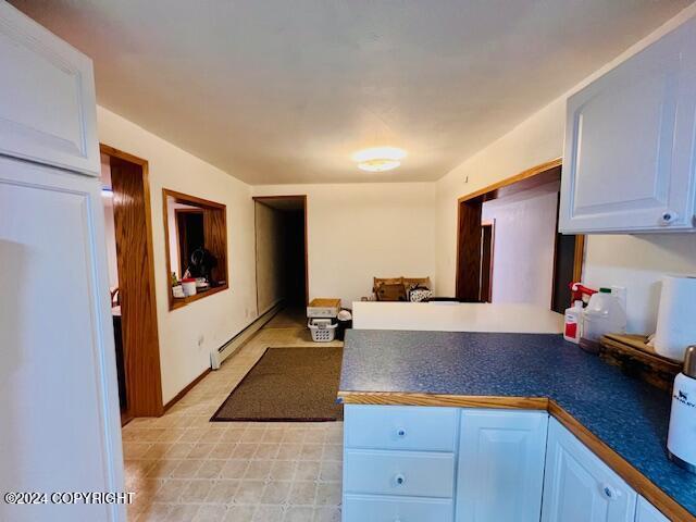 3411 Monashka Bay Rd, Kodiak, AK 99615 - kitchen featuring a baseboard radiator, a peninsula, dark countertops, light flooring, and white cabinetry