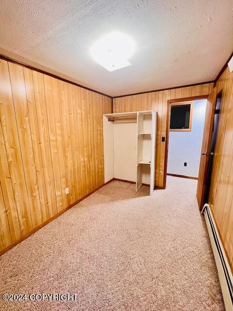 3411 Monashka Bay Rd, Kodiak, AK 99615 - unfurnished bedroom with a baseboard radiator, wooden walls, light colored carpet, and a textured ceiling