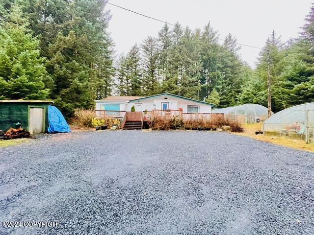 view of front of home with gravel driveway, a wooden deck, an outbuilding, and an exterior structure