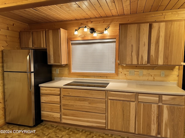 kitchen featuring wooden walls, black electric stovetop, and stainless steel refrigerator