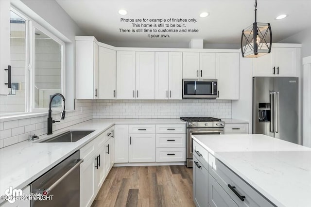 kitchen with sink, light stone counters, premium appliances, pendant lighting, and white cabinets