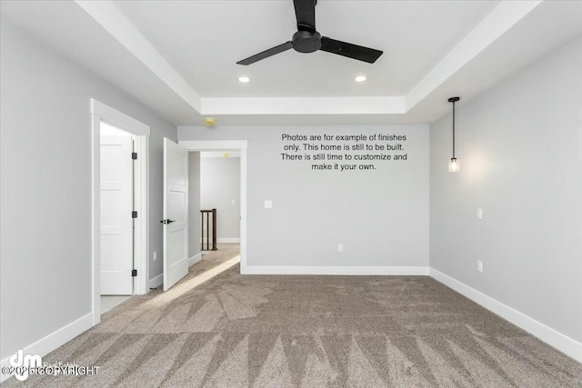 empty room featuring a tray ceiling, ceiling fan, and carpet