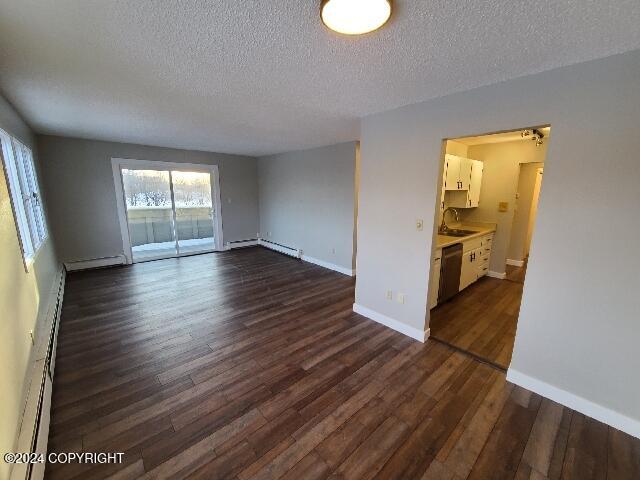 unfurnished room featuring a textured ceiling, sink, a baseboard radiator, and dark hardwood / wood-style floors