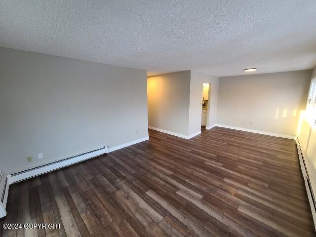 unfurnished room with a textured ceiling, dark hardwood / wood-style flooring, and a baseboard heating unit