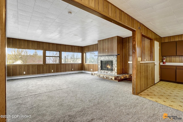 unfurnished living room featuring a baseboard heating unit, a stone fireplace, wooden walls, and carpet flooring