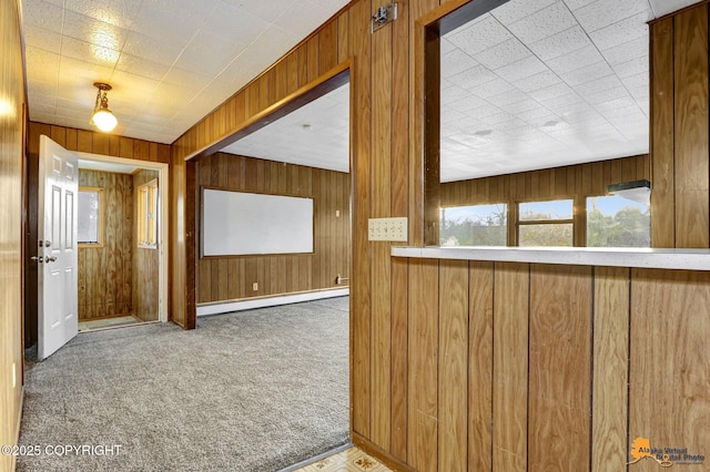 hall featuring baseboard heating, wood walls, and carpet floors