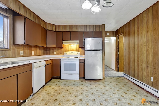 kitchen with under cabinet range hood, baseboard heating, white appliances, and wooden walls