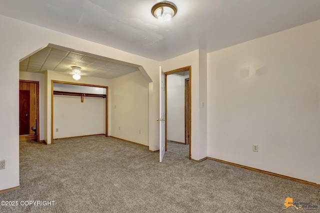 unfurnished bedroom with a closet, arched walkways, baseboards, and carpet flooring