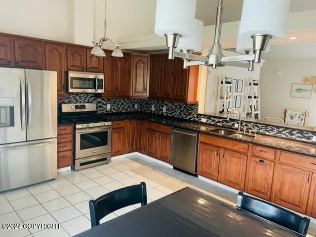 kitchen with sink, backsplash, pendant lighting, light tile patterned floors, and appliances with stainless steel finishes