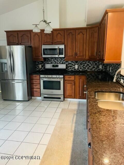 kitchen with appliances with stainless steel finishes, light tile patterned floors, lofted ceiling, and sink