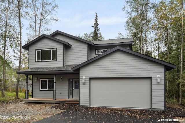 view of front of house with covered porch, asphalt driveway, a garage, and a shingled roof