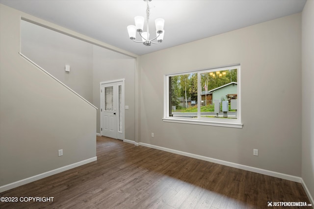 empty room with a chandelier, wood finished floors, and baseboards
