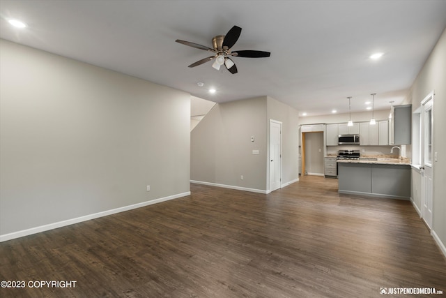 unfurnished living room featuring a ceiling fan, recessed lighting, dark wood finished floors, baseboards, and a sink