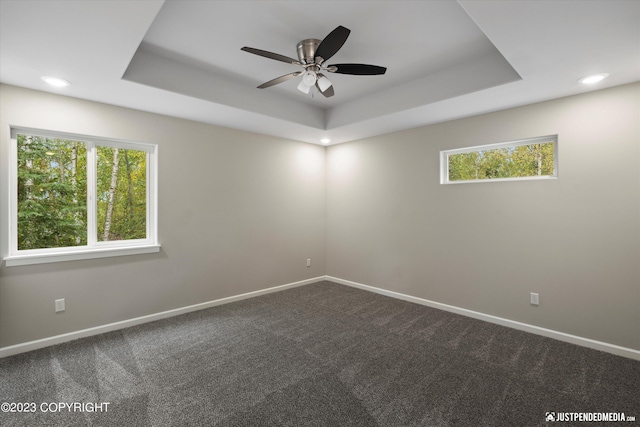 empty room with a raised ceiling, baseboards, dark colored carpet, ceiling fan, and recessed lighting