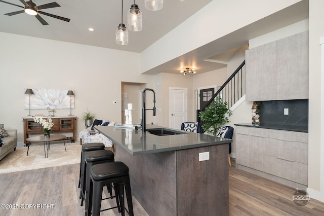 kitchen with ceiling fan, sink, backsplash, decorative light fixtures, and light wood-type flooring