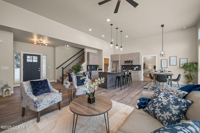 living room with a towering ceiling, light wood-type flooring, ceiling fan, and sink