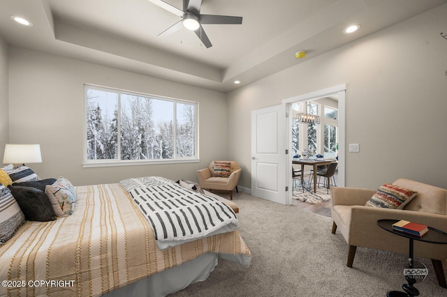 bedroom featuring a tray ceiling, multiple windows, carpet, and ceiling fan with notable chandelier