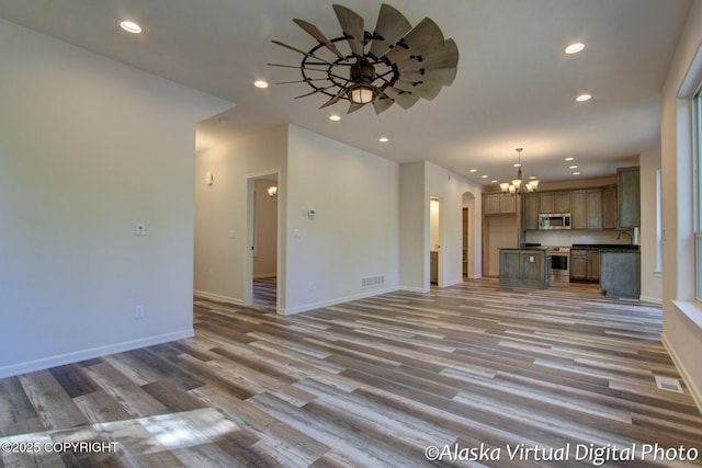 unfurnished living room featuring light hardwood / wood-style flooring, ceiling fan with notable chandelier, and sink