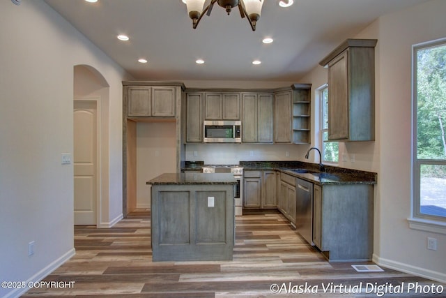 kitchen with appliances with stainless steel finishes, dark stone countertops, a notable chandelier, and sink